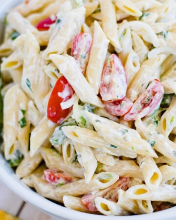 overhead photo of a white glass serving bowl filled with a pasta salad made with tomatoes and fresh asparagus