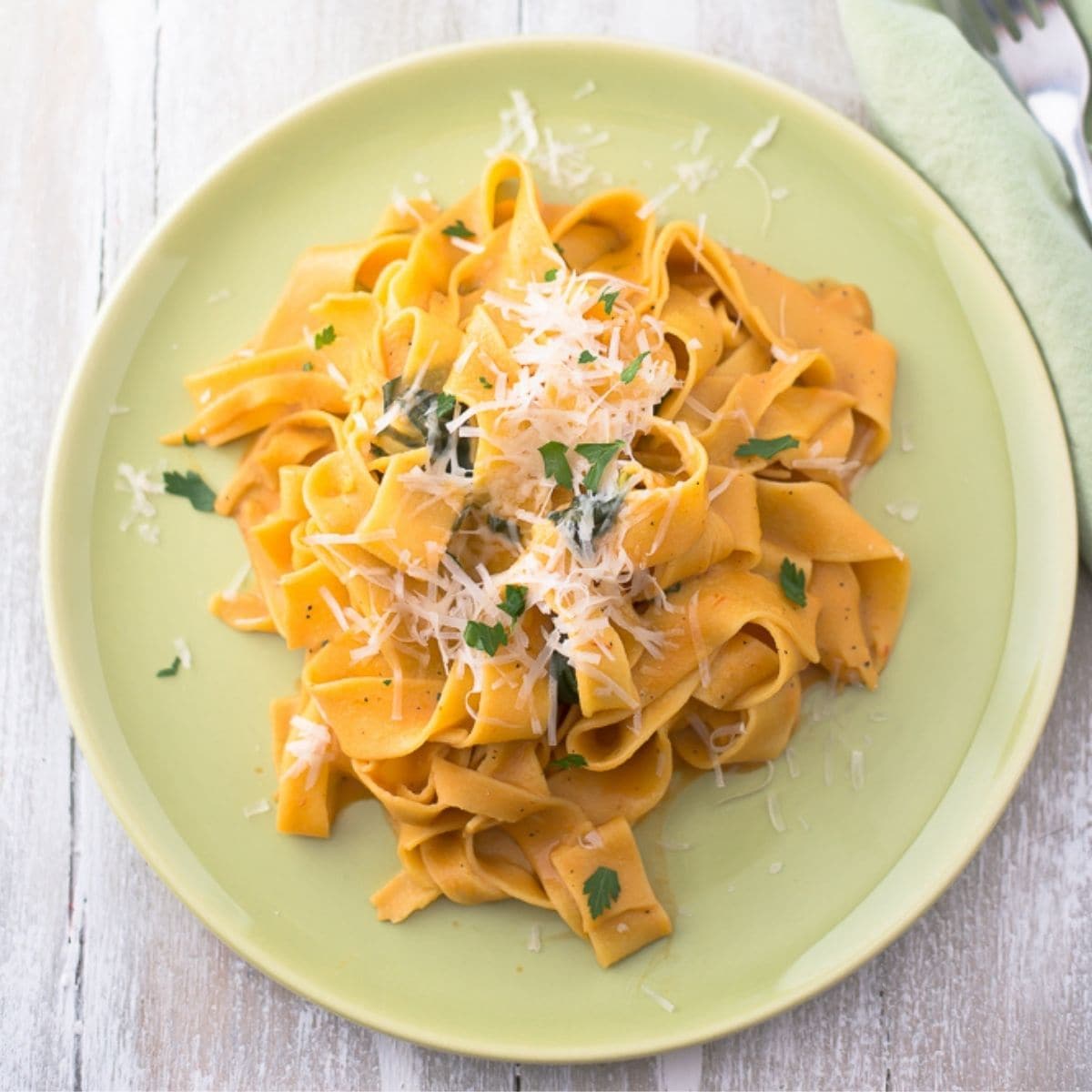 Vegetarian Pappardelle with butternut squash sauce served on a green dinner plate.