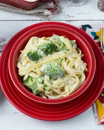 Broccoli Fettuccine Alfredo served in a red bowl with bread and salad.