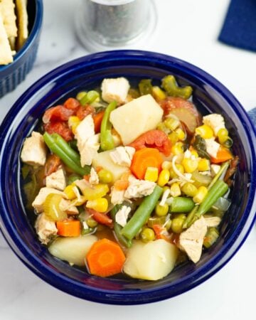 Chicken and Veggie soup served in a blue bowl with crackers.
