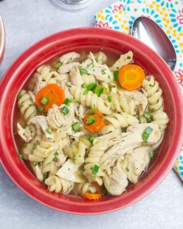 Red bowl filled with Crock Pot Spicy Chicken Noodle Soup garnished with parsley.